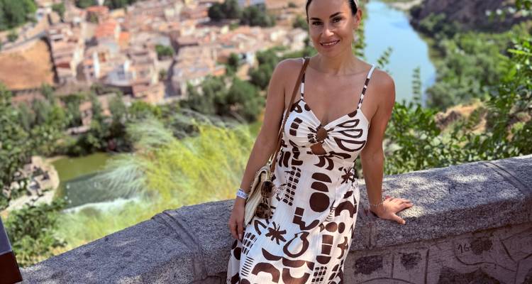 Femme appuyée sur une clôture de pierre avec un arrière-plan pittoresque d'une ville au bord d'une rivière.