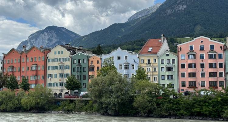 Rangée de bâtiments colorés le long d'une rivière avec des montagnes.