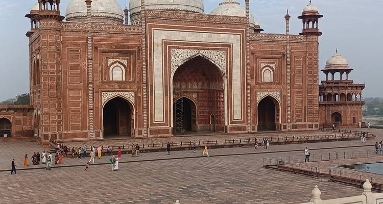 Cour de mosquée en grès rouge avec des gens qui marchent.