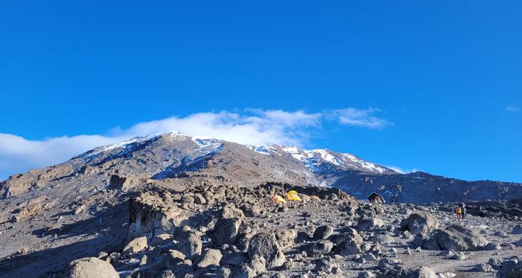 Rocky terrain leading to snow-capped mountains under clear blue sky.