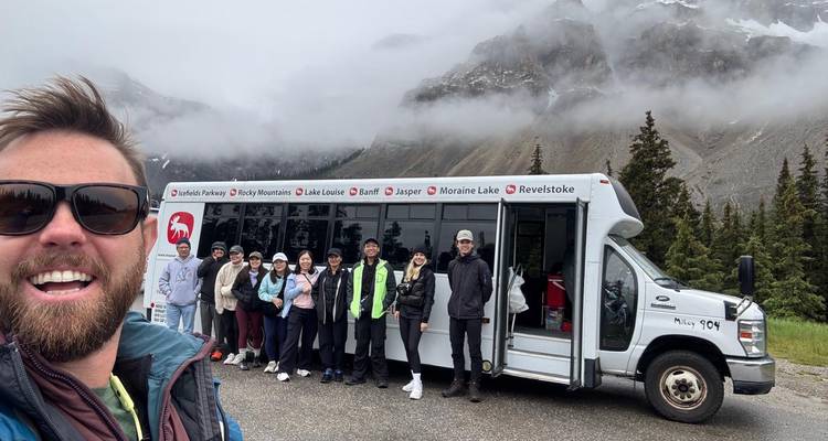 Groupe de touristes debout devant un véhicule de visite avec des montagnes en arrière-plan.