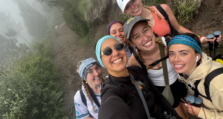 Group of smiling hikers posing on a foggy mountain trail.