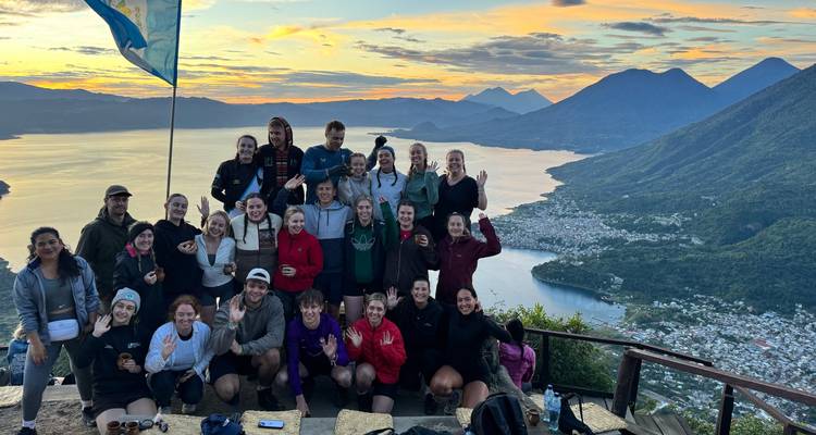 Large group photo with a view of a lake and mountains during sunset.