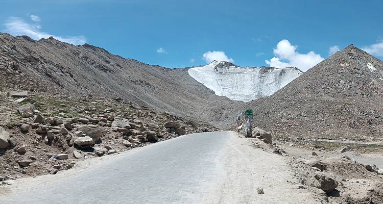Straße, die zu Bergen mit einem Gletscher im Hintergrund führt.