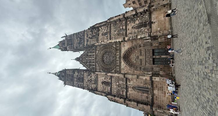 Grande église de style gothique avec deux tours et une rosace, des gens devant.