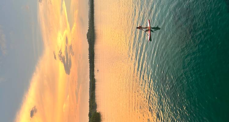 Personne faisant du paddle sur une eau calme avec un coucher de soleil vibrant en arrière-plan.