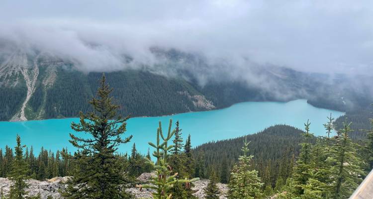 Une vue d'un lac turquoise entouré de montagnes partiellement voilées de nuages.