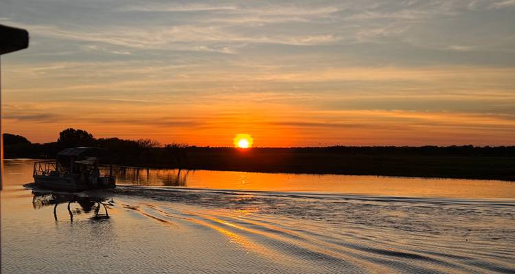 Sunset over a river with a silhouette of a boat.