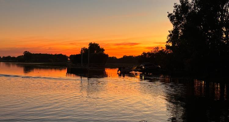 Coucher de soleil sur un lac avec des arbres en silhouette.