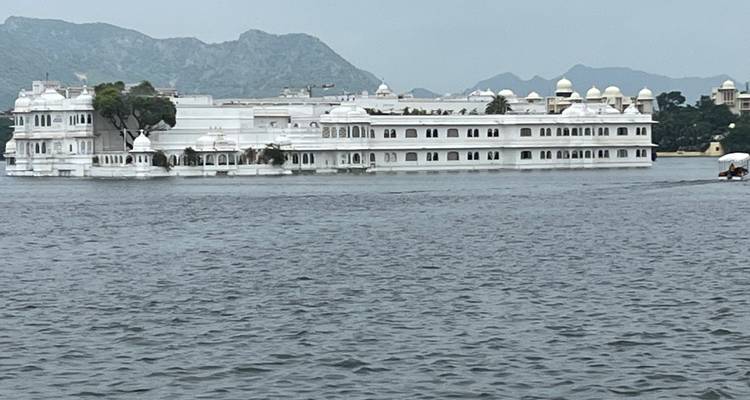 Grand palais blanc sur un lac avec des montagnes en arrière-plan.