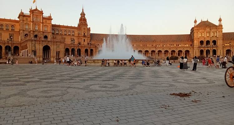 Une grande place avec une fontaine et un bâtiment imposant, des gens qui se promènent.