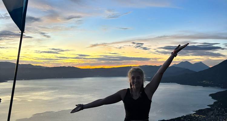 Personne posant les bras ouverts devant un lac au coucher du soleil.