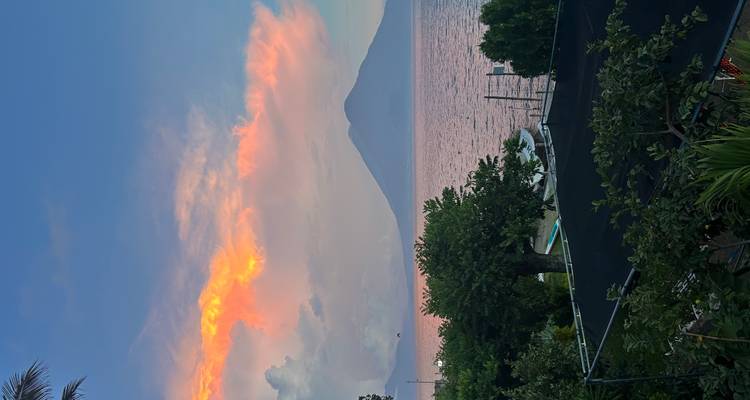 View of a volcano across a lake at sunset, with vibrant sky colors.