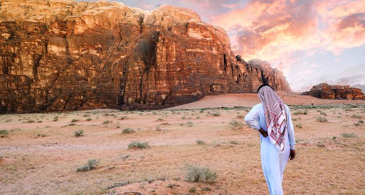 Personne en tenue traditionnelle debout devant des formations rocheuses spectaculaires au coucher du soleil.