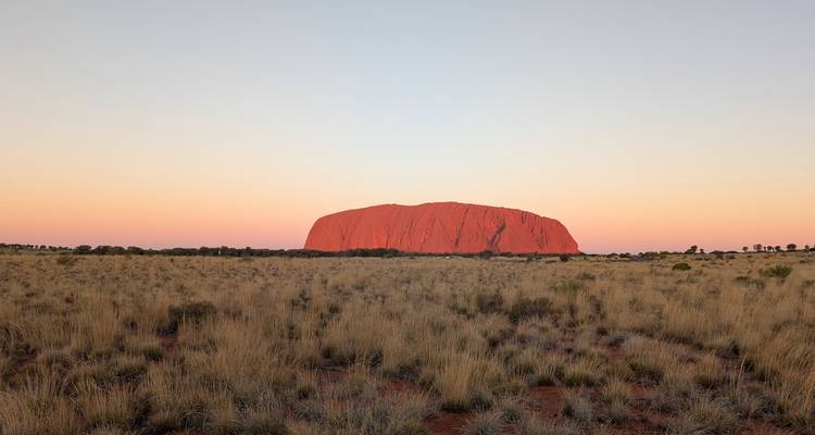 Uluru unter dem warmen Schein eines Sonnenuntergangshimmels.