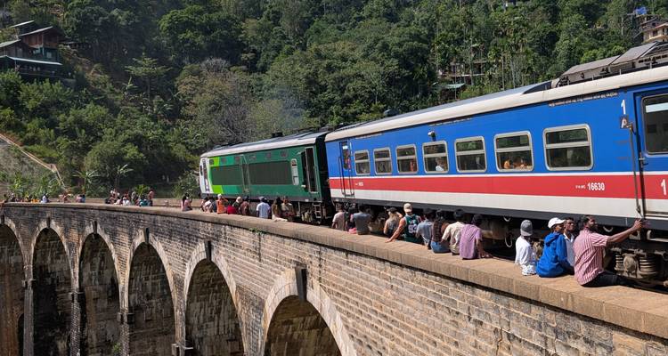 A train crossing a historic stone bridge with people sitting along the sides.