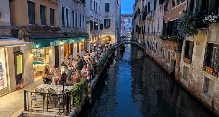 An evening canal scene in Venice with people dining by the water.