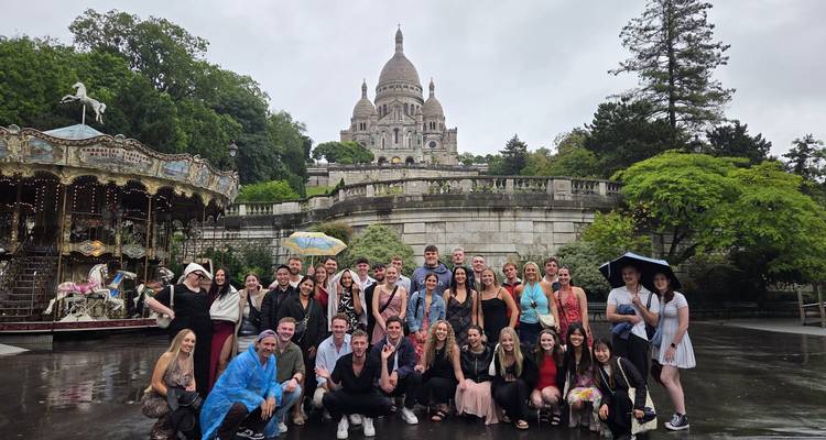 Large group posing in front of Sacré-Cœur Basilica under cloudy skies.