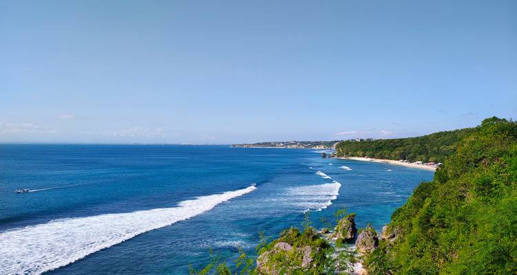 Luftaufnahme einer Küstenlinie mit Wellen und grünen Hügeln.