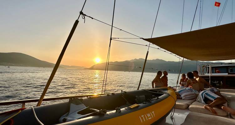 Voilier au coucher de soleil avec des personnes se relaxant sur le pont.
