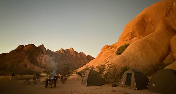 Camping site at dusk with tents and rock formations.