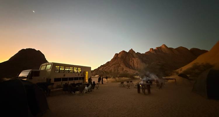 Camping site with a large safari truck and rock formations at sunset.