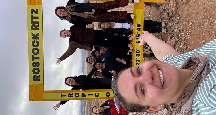 Group posing with a Tropic of Capricorn signboard in a desert.