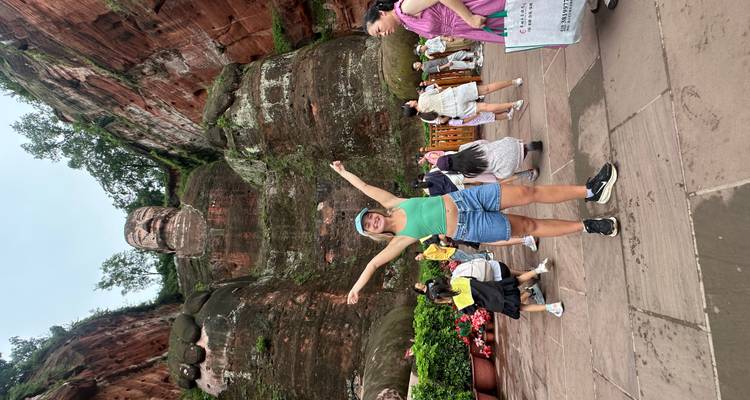 Une femme posant devant le Grand Bouddha de Leshan avec d'autres touristes autour.