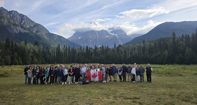 Large group photo in front of mountainous landscape with a Canadian flag.
