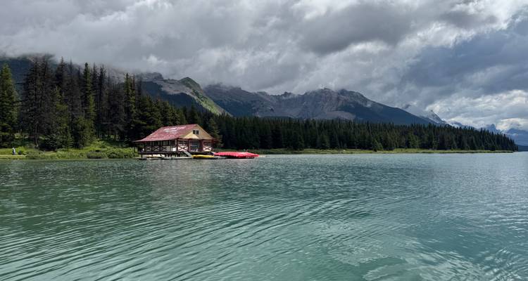 Wooden lodge by a lake surrounded by forested mountains.