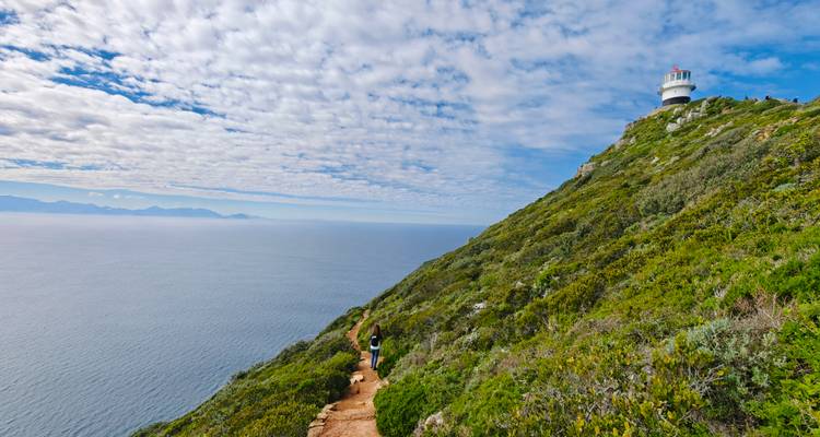 A scenic view of a lighthouse on a hill overlooking the ocean.