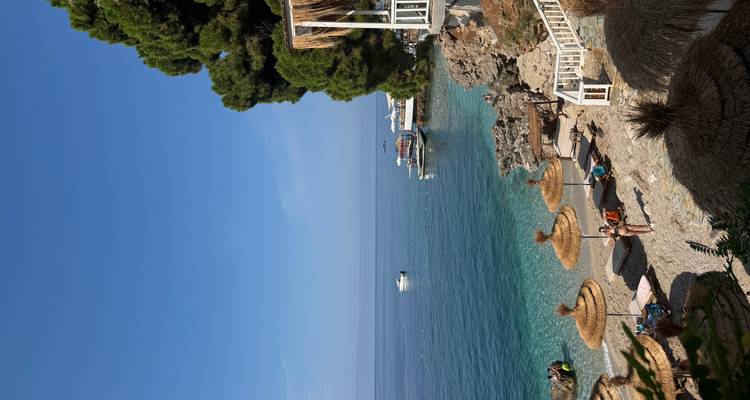 Beach with sun loungers and umbrellas, overlooking clear blue sea.