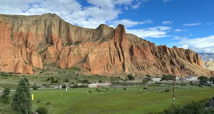 Rocky cliffs with green fields and small structures.