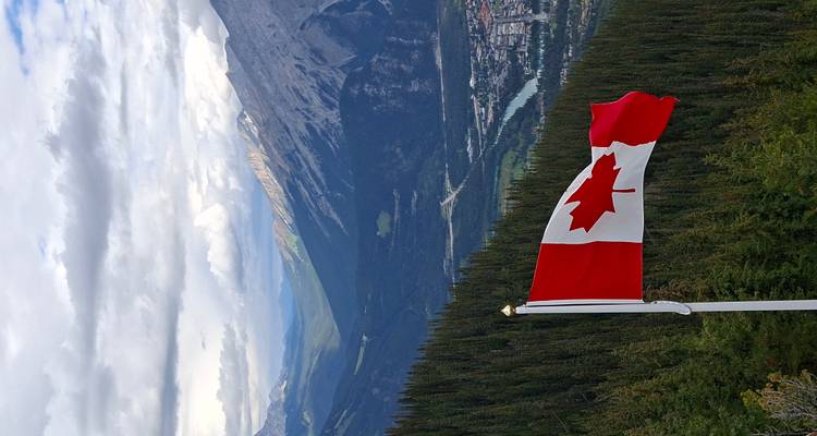 Canadian flag overlooking a valley surrounded by mountains.