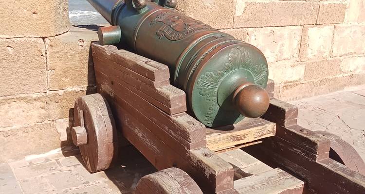 Un cañón histórico sobre un carruaje de madera contra una pared de piedra.