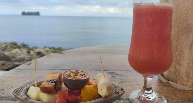 Plate of tropical fruits and a drink, with a lake view.