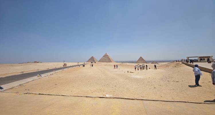Panoramic view of the Pyramids of Giza with tourists in the foreground under a clear blue sky.