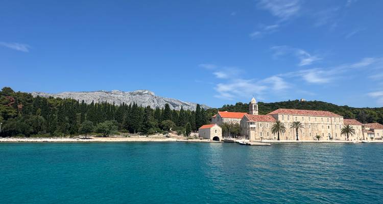 Paysage côtier pittoresque avec un bâtiment historique et des montagnes.