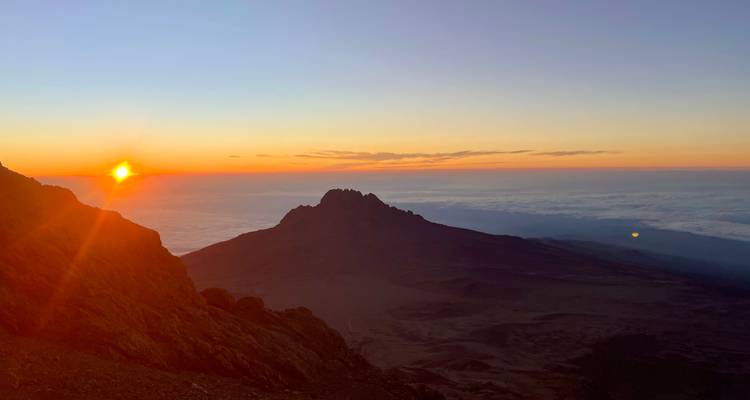 Paysage du Kilimandjaro au lever du soleil avec des pics spectaculaires et une couverture nuageuse.