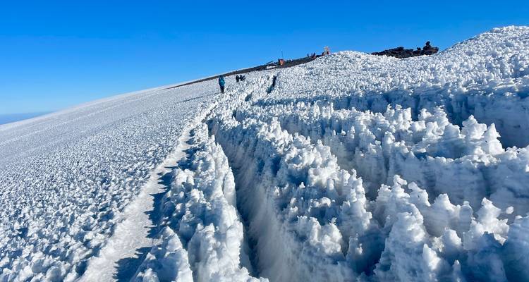 Sentier de montagne enneigé avec des grimpeurs au loin.
