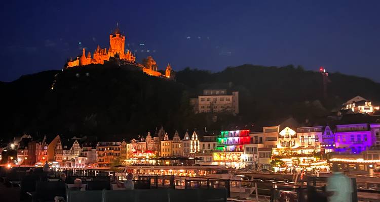 Night view of a castle and vibrant town lights reflecting on a river.