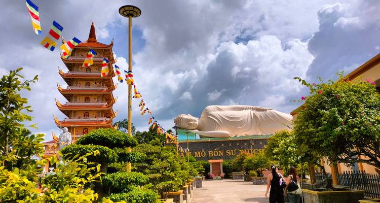 Statue de Bouddha couché à côté d'une pagode sous un ciel nuageux.