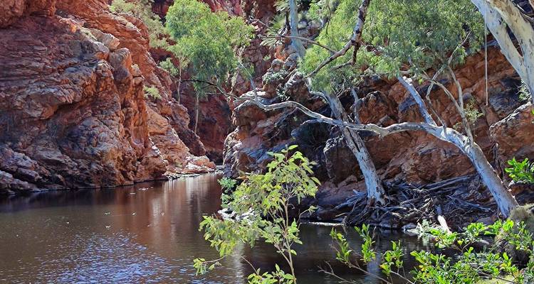 Vue d'un plan d'eau entre des formations rocheuses rouges et des arbres.