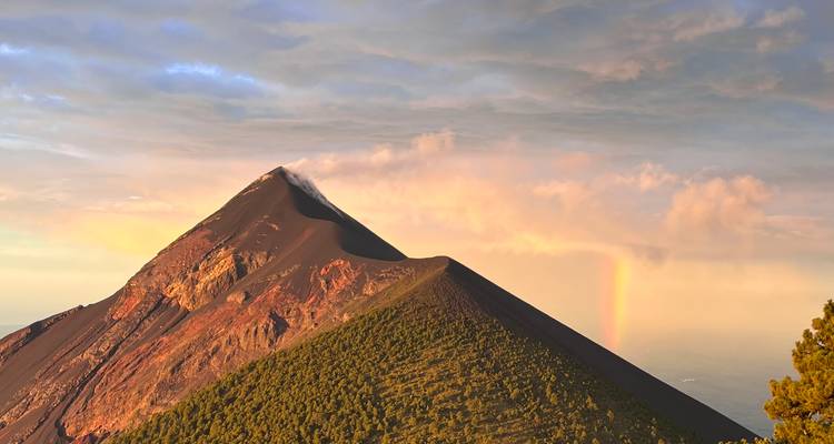 Eine Vulkanlandschaft mit einem Regenbogen und Sonnenuntergang.