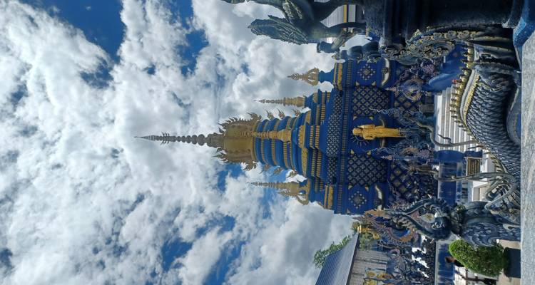 Elaborado templo azul con estatuas doradas bajo un cielo nublado.