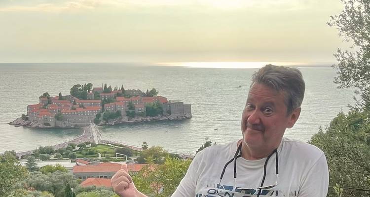 A man gesturing towards Sveti Stefan Island with the sea beyond.