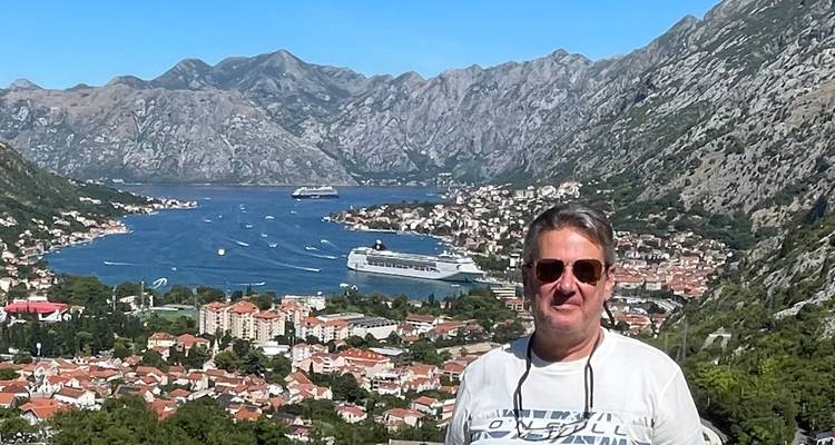 A man standing with a view of Kotor Bay and the mountains.