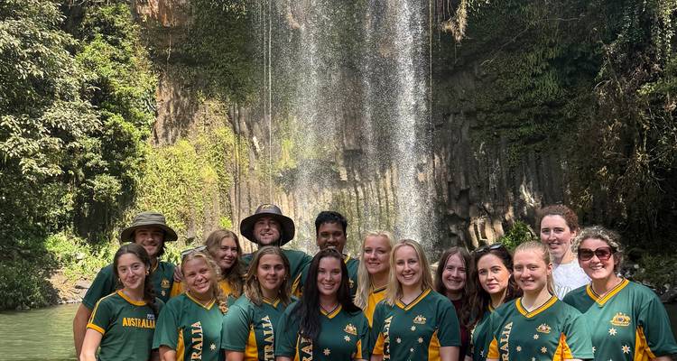 Grupo de personas en camisetas australianas posando frente a una cascada.