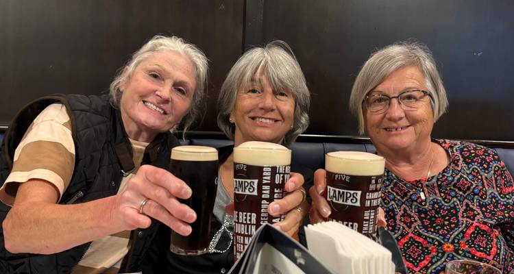 Trois femmes levant des verres de bière brune dans un cadre de pub.
