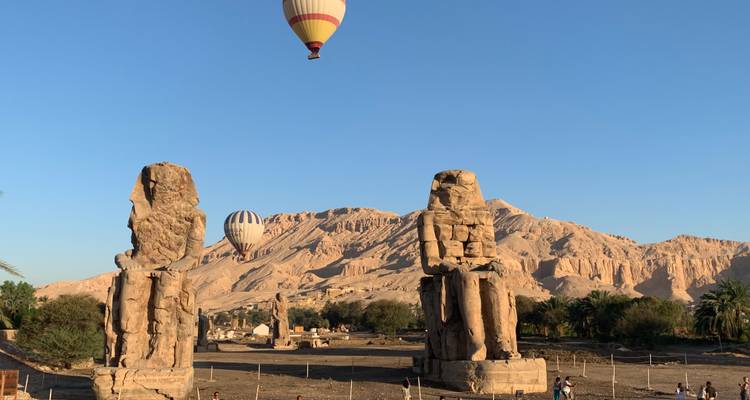 Two giant stone statues with hot air balloons overhead.